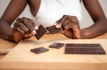 front view of an unrecognizable african american Woman Breaking a Bar of Dark Chocolate into Pieces...
