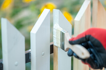 Close up of man hand in protective glove painting fence in white color. Painting new wooden fence...