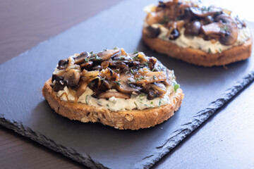 delicious mushroom toast with herb cream cheese, mushrooms, and caramelized onions on a black stone plate close-up