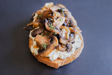 delicious mushroom toast with herb cream cheese, mushrooms, and caramelized onions on a black stone plate close-up