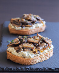 delicious mushroom toast with herb cream cheese, mushrooms, and caramelized onions on a black stone plate close-up