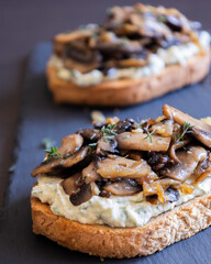 delicious mushroom toast with herb cream cheese, mushrooms, and caramelized onions on a black stone plate close-up