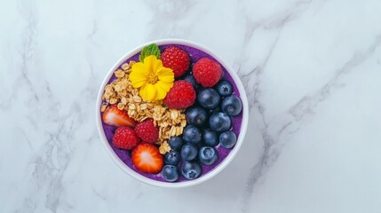 Vibrant acai bowl with fresh berries, granola, and edible flower on marble background - healthy breakfast concept
