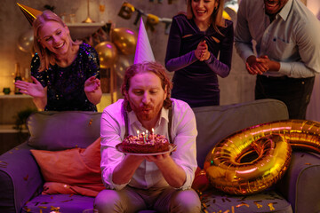 Man blowing candles on birthday cake celebrating with friends