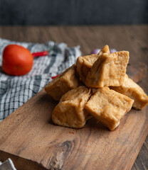 Fried tofu stacked on a wooden cutting board, surrounded by fresh chili, garlic, shallots, and tomatoes on a rustic kitchen table. Perfect for culinary, food, and cooking concepts.