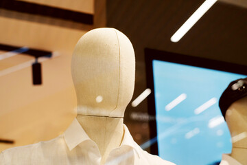 Close-up portrait of a faceless mannequin in a clothing store window behind glass, glare on glass,...