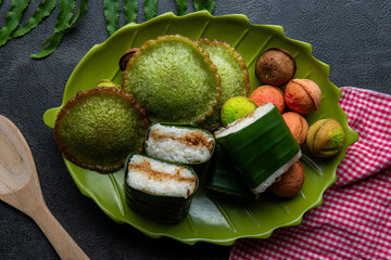 A plate of authentic Indonesian market snacks, featuring lemper wrapped in banana leaves, green kue...