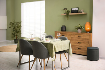 Fototapeta premium Stylish table setting with olive tablecloth, glasses and candles in dining room