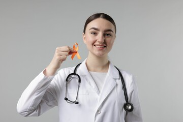 Multiple Sclerosis awareness. Happy doctor holding orange ribbon on light grey background