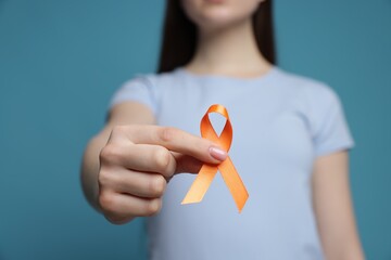 Multiple Sclerosis awareness. Young woman holding orange ribbon on light blue background, closeup