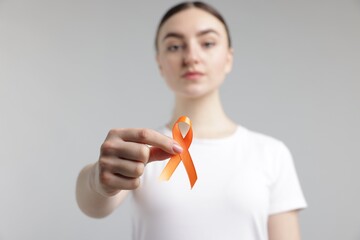 Multiple Sclerosis awareness. Young woman holding orange ribbon on light grey background, selective...