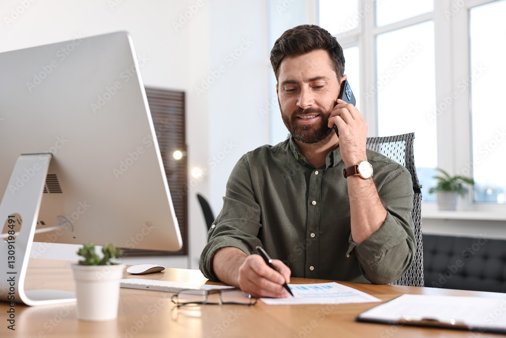Poster man talking on smartphone while working at table in office