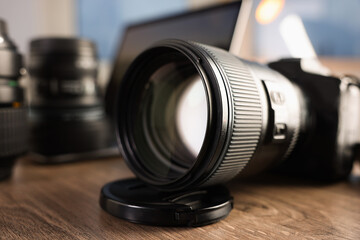 Professional photo camera, lenses and laptop on wooden desk indoors, selective focus