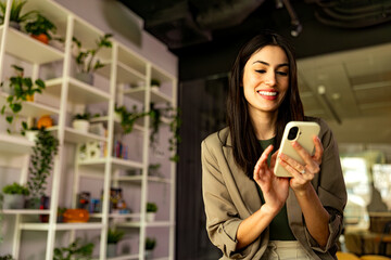 A businesswoman sitting in a bright, spacious co-working environment, texting on her smartphone.
