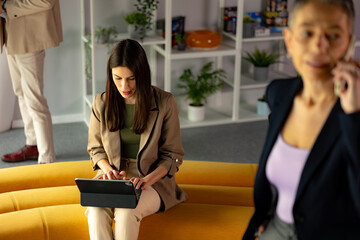 A young woman is working on her tablet in a modern coworking space. Other business people around