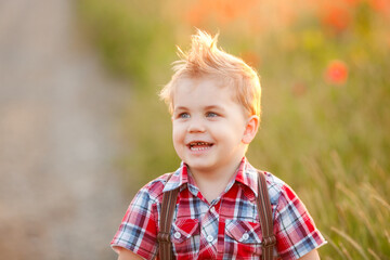A cheerful small boy with crossed eyes laughing and grinning in a poppy meadow during sunset
