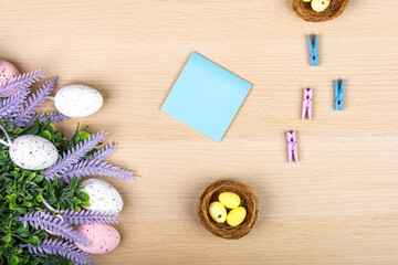 Easter eggs on a wooden background, top view, flatlay, painted quail eggs in a nest, place for text - sheet of paper, copy space, Easter concept, some little Stationery clothespins.Education concept