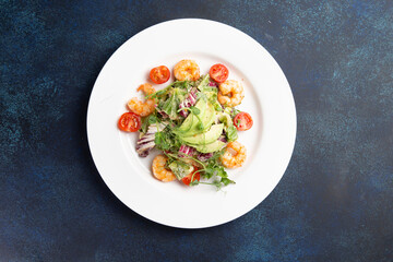 Salad with shrimps and avocado in a plate on a dark background.