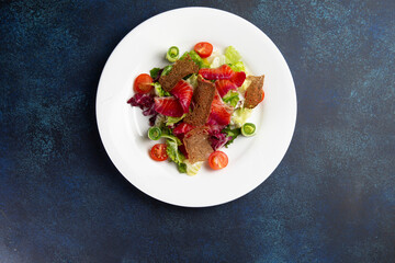 Salad with salmon in a plate on a dark background.