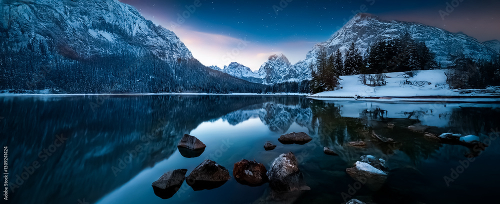 Poster snowy mountains reflect in a tranquil lake beneath a twilight sky. rocks dot the foreground in this 