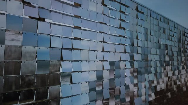 A wall of reflective rows of plexiglass panels moving in tandem with a fast wind, wide shot