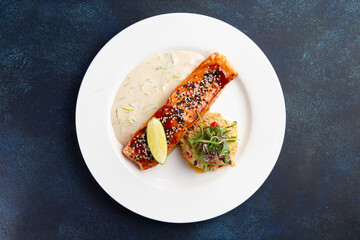 Salmon steak and rice in a plate on a dark background.