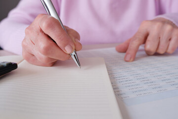 Senior woman writing notes while reviewing financial documents