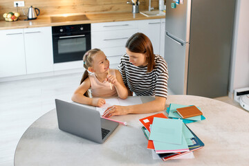 Mother and daughter engage in homework together at kitchen table during afternoon study session