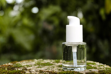A close-up of a transparent glass pump bottle with a white dispenser cap, placed on a moss-covered...