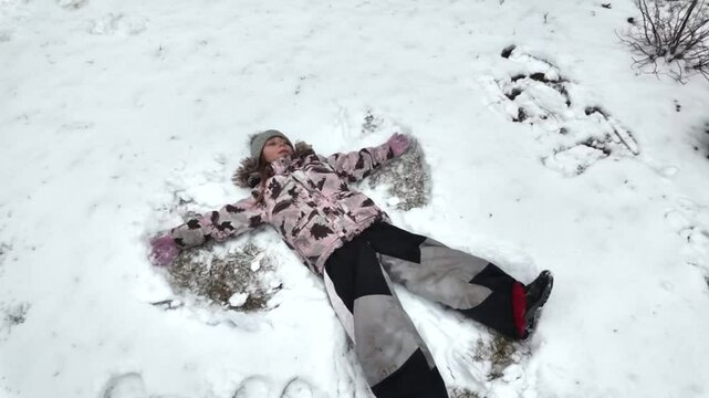 Happy child playing in the snow making an angel on the street