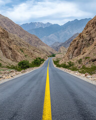 Fototapeta premium A winding road stretches through a rocky landscape, flanked by mountains under a cloudy sky, inviting adventure and exploration.