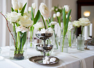 wedding table setting with desserts and spring white flowers in vases in white room