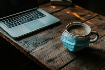 Coffee Cup with Face Mask Beside Laptop on Wooden Table