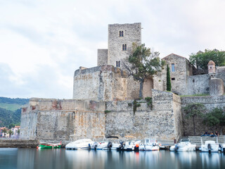 Construcción medieval al lado de un puerto con barcas amarradas y cielo nuboso del atardecer.