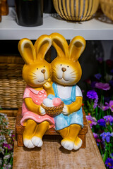 Easter bunny figurine with basket of colorful eggs. Pair of Easter bunny figurines with basket of colorful eggs, surrounded by artificial flowers. Bright cheerful spring decoration