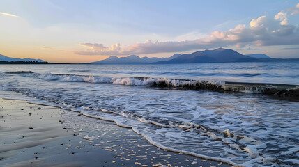 A scenic view of a beach at evening, with gentle sea waves, distant mountains, and a tranquil sunset sky.