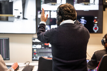 A television director in a broadcast control room, actively guiding a live production. Surrounded...