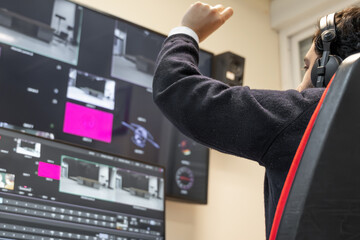 A television director in a broadcast control room, actively guiding a live production. Surrounded...