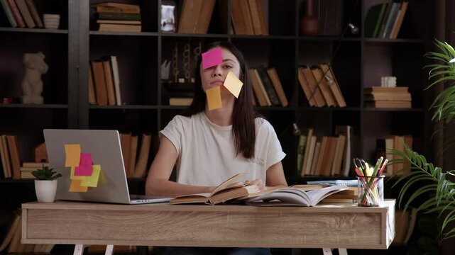 Tired student with many colorful stickers stuck on her face with tasks to complete. Exhausted young woman with her head on the office table. Concept of studies, projects, exams, students.