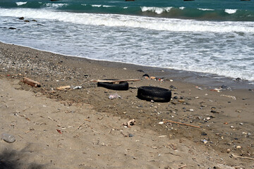 Various types of garbage, including plastic bottles, tires, and other hazardous waste, are scattered on the beach in Greece.