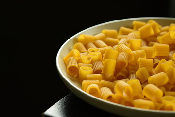 raw pasta on a white plate against black backdrop