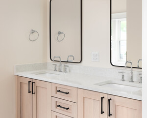 A bathroom detail with a natural wood cabinet, white marble countertop, chrome faucet, and black...