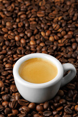 Small white espresso cup, nestled among bed of roasted coffee beans, creating cozy and inviting atmosphere perfect for enthusiasts