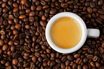Top view of small espresso cup stands on roasted beans, highlighting rich crema and creating perfect background for coffee lovers