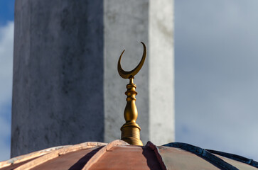 A golden crescent moon finial sits atop a dome, with a minaret in the background. The image captures the details of Islamic architectural ornamentation.