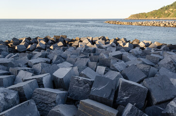 Rocks meet the sea. Breakwater texture. Coastal scene. Horizon line. Light and shadow play.