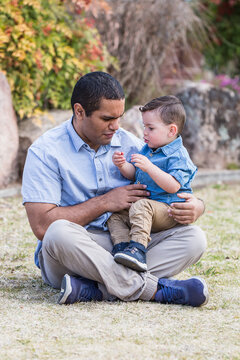 Mixed race aboriginal caucasian son sitting on dad's lap talking
