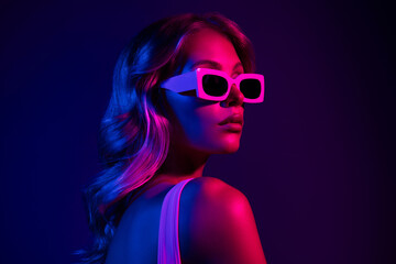 Alluring young woman with blond hair in neon pink light against dark purple background
