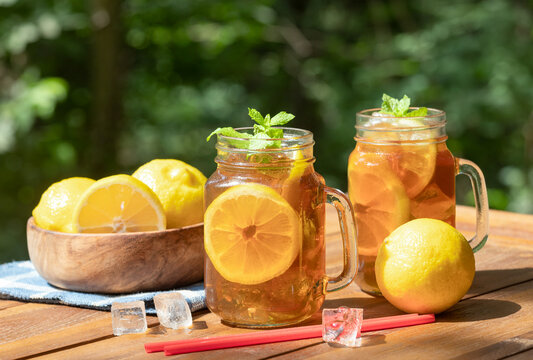 Ice tea with lemon slices and mint outdoors on wooden table