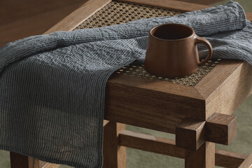 Brown ceramic cup on rattan stool with linen tea towel.